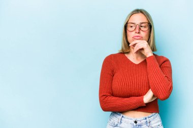 Mavi arka planda soyutlanmış beyaz bir kadın şüpheli ve şüpheci bir ifadeyle yana bakıyor..