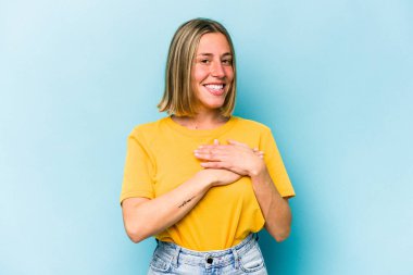 Mavi arka planda izole edilmiş beyaz bir kadın, dost canlısı bir ifadeye sahip, avuçlarını göğsüne bastırıyor. Aşk konsepti.