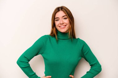 Beyaz arka planda izole edilmiş beyaz tenli genç bir kadın ellerini kalçasından ayırmıyor..