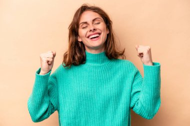 Beyazlı genç bir kadın bej arka planda izole edilmiş zafer, tutku ve coşkuyu kutluyor, mutlu bir ifade..