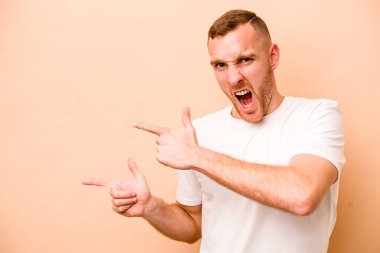 Beyaz tenli genç adam bej arka planda izole edilmiş ve işaret parmağıyla fotokopi alanını işaret ederek heyecan ve arzusunu ifade ediyor..