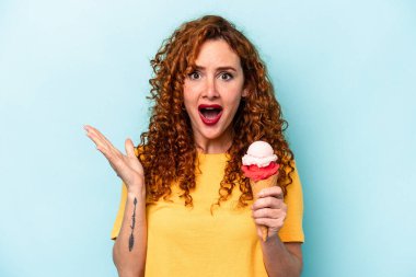 Mavi arka planda izole edilmiş dondurmayı tutan kızıl saçlı genç kadın şaşırdı ve şok oldu..