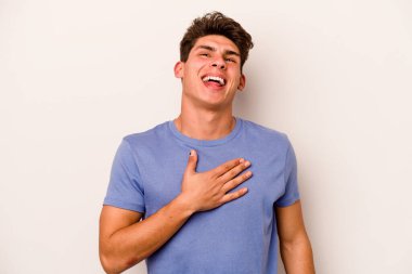Beyaz arka planda izole genç beyaz adam yüksek sesle gülüyor elini göğsüne koyuyor..