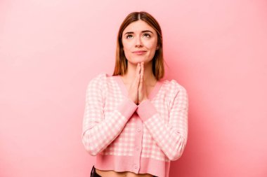Pembe arka planda soyutlanmış genç beyaz bir kadın el ele tutuşup ağzının kenarında dua ediyor, kendinden emin hissediyor..