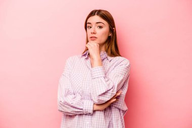 Pembe arka planda izole edilmiş genç beyaz kadın şüpheli, belirsiz, seni muayene ediyor..