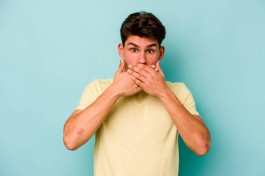 Kafkasyalı genç adam mavi arka planda izole edilmiş ağzı kapalı ve elleri endişeli görünüyor..