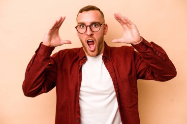 Beyaz tenli genç adam bej arka planda izole edilmiş. Hoş bir sürpriz bekliyor. Heyecanlı ve el kaldırıyor..