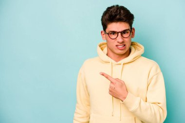 Mavi arka planda izole edilmiş genç beyaz adam yan tarafı işaret ediyor.