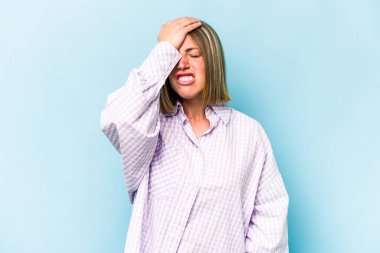 Kafkasyalı genç bir kadın mavi arka planda izole edilmiş bir şekilde bir şeyi unutuyor. Alnına avuç içi ve gözlerini kapayarak vuruyor..