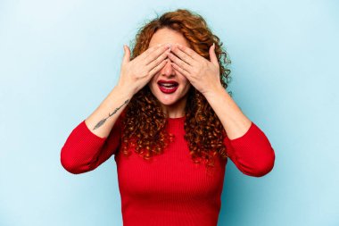 Mavi arka planda izole edilmiş genç, beyaz kadın elleriyle gözlerini kapatmaktan korkuyor..