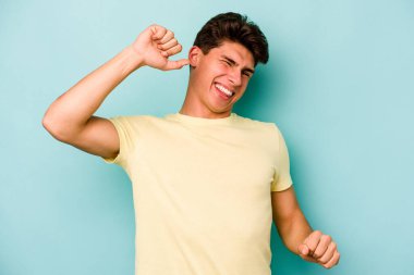 Mavi arka planda izole genç beyaz adam özel bir günü kutluyor, atlıyor ve enerjiyle kollarını kaldırıyor..