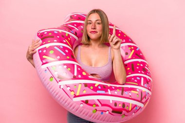 Elinde şişme yatak tutan beyaz bir kadın pembe arka planda izole edilmiş bir şekilde parmak iziyle bir numarayı gösteriyor..