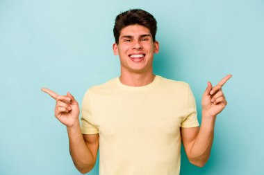 Mavi arka planda izole edilmiş genç beyaz adam farklı kopya alanlarını gösteriyor, birini seçiyor, parmaklarıyla gösteriyor.