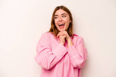 Beyaz arka planda izole edilmiş genç beyaz kadın ellerini çenesinin altında tutuyor, mutlu bir şekilde yana bakıyor..