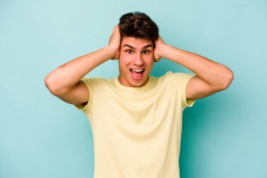 Genç beyaz adam mavi arka planda izole edilmiş bağırıyor, çok heyecanlı, tutkulu, bir şeyden memnun..