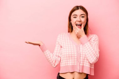 Pembe arka planda izole edilmiş genç beyaz kadın avuç içinde fotokopi alanı tutuyor, el üstünde tutuyor. Şaşırmış ve mutlu..