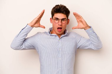 Beyaz arka planda izole olmuş genç beyaz bir adam zaferi veya başarıyı kutluyor, şaşırıyor ve şok oluyor..