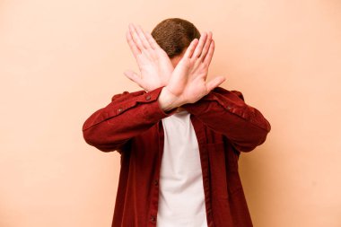 Beyazlı genç adam bej arka planda izole edilmiş iki kolu çapraz tutuyor, inkar kavramı.