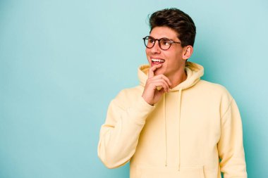 Mavi arka planda izole edilmiş genç beyaz adam rahatlamış bir şeyin fotokopi odasına baktığını düşünüyor..