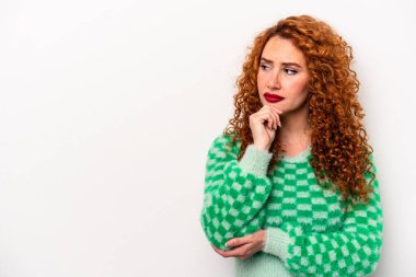 Beyaz arka planda soyutlanmış beyaz tenli genç bir kadın şüpheli ve şüpheci bir ifadeyle yana bakıyor..