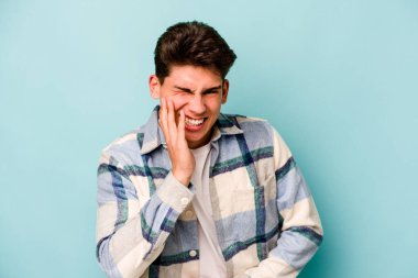 Mavi arka planda izole edilmiş genç beyaz adam mutlu bir şekilde gülüyor ve ellerini karnının üstünde tutarak eğleniyor..