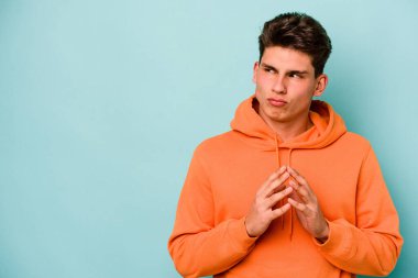 Kafkasyalı genç bir adam mavi arka planda izole edildi. Aklında bir plan kuruyor, bir fikir kuruyor..