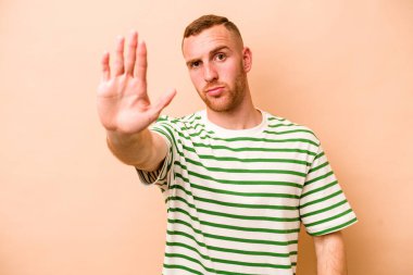 Beyazlı genç bir adam bej arka planda izole edilmiş, elini uzatmış, dur işareti göstererek seni engelliyor..