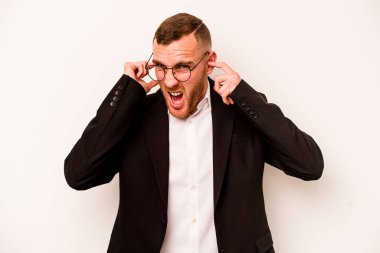 Beyaz arka planda izole edilmiş genç bir beyaz adam kulaklarını elleriyle kapatıyor..