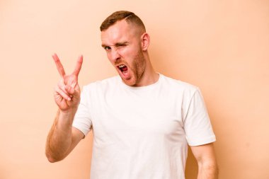 Beyazlı genç bir adam bej arka planda izole edilmiş. İki numarayı parmaklarıyla gösteriyor..