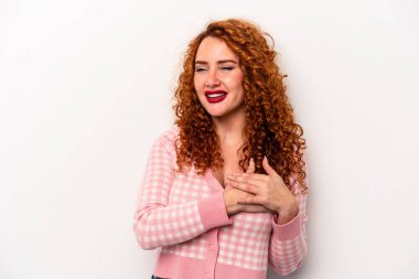 Beyaz arka planda soyutlanmış beyaz tenli genç bir kadın gülüyor, elini kalbe koyuyor, mutluluk kavramını koruyor..