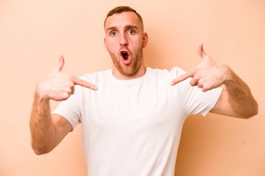 Beyazlı genç bir adam bej arka planda izole edilmiş. Parmakları aşağıda, olumlu hisler içinde..