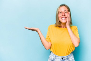 Mavi arka planda izole edilmiş beyaz bir kadın avuç içinde fotokopi alanı tutuyor, el üstünde tutuyor. Şaşırmış ve mutlu..