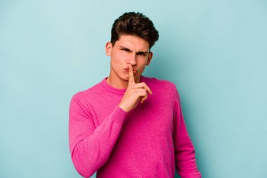 Mavi arka planda izole edilmiş genç beyaz bir adam ya sır saklıyor ya da sessizlik istiyor..