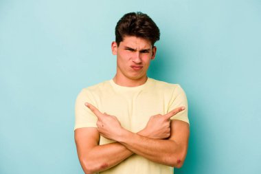 Mavi arka plan noktalarında izole genç beyaz adam, iki seçenek arasında seçim yapmaya çalışıyor.