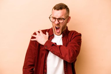 Beyaz tenli genç adam bej arka planda izole edilmiş, omuz ağrısı var..