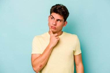 Kafkasyalı genç bir adam mavi arka planda izole edilmiş. Bir strateji planlıyor, bir iş yolu düşünüyor..