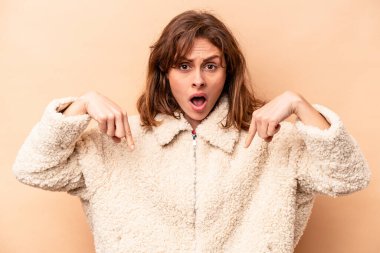 Beyaz tenli genç bir kadın bej arka planda izole edilmiş. Parmakları aşağıda, olumlu hisler içinde..