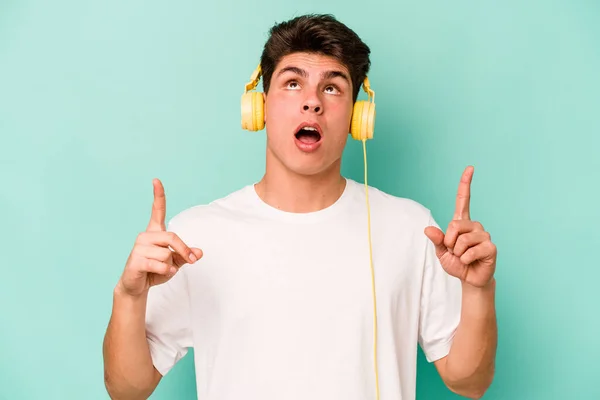 Jonge Kaukasische Man Luisteren Naar Muziek Geïsoleerd Blauwe Achtergrond Wijzend — Stockfoto
