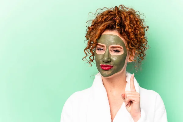 Young red hair woman with a facial aloe vera mask after a bath isolated showing number one with finger.