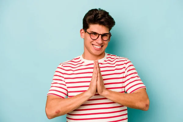 Young Caucasian Man Isolated Blue Background Holding Hands Pray Mouth — Stock Photo, Image