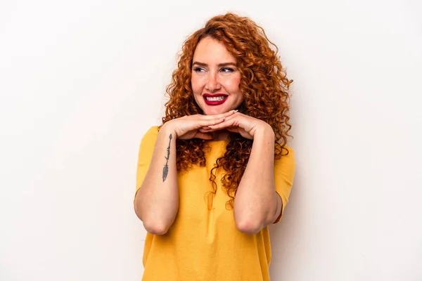 Young ginger caucasian woman isolated on white background keeps hands under chin, is looking happily aside.