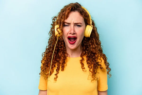 Νεαρή Κοκκινομάλλα Που Ακούει Μουσική Απομονωμένη Μπλε Φόντο Ουρλιάζοντας Πολύ — Φωτογραφία Αρχείου