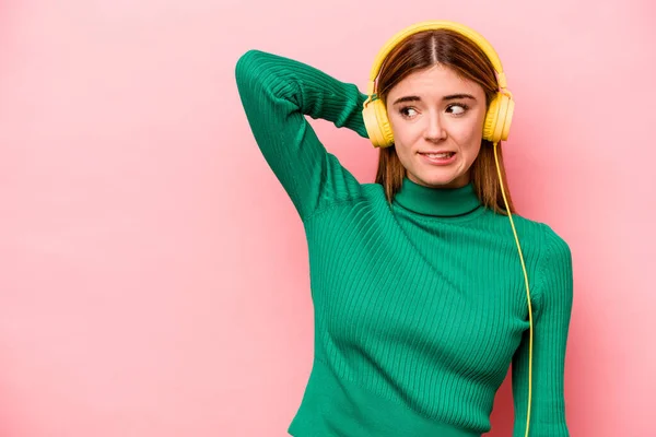 Young caucasian woman listening to music isolated on pink background touching back of head, thinking and making a choice.