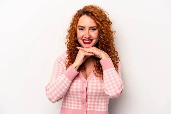 Young ginger caucasian woman isolated on white background keeps hands under chin, is looking happily aside.
