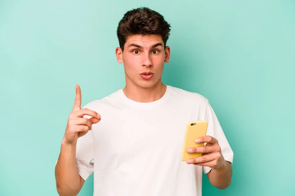 Młody Biały Mężczyzna Trzymając Telefon Komórkowy Niebieskim Tle Mając Jakiś — Zdjęcie stockowe