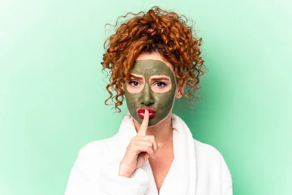 Young red hair woman with a facial aloe vera mask after a bath isolated keeping a secret or asking for silence.