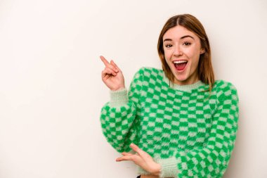 Beyaz arka planda izole edilmiş beyaz tenli genç bir kadın işaret parmağıyla işaret ederek heyecanlanıyor..
