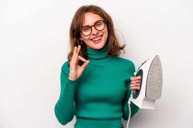 Beyaz arka planda demir tutan genç beyaz kadın neşeli ve kendinden emin, iyi bir hareket sergiliyor..