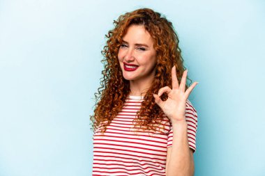 Genç, beyaz, mavi arka planda izole edilmiş, neşeli ve kendinden emin bir kadın..