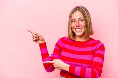 Pembe arka planda izole edilmiş genç beyaz kadın işaret parmaklarıyla işaret ederek heyecanlanıyor..